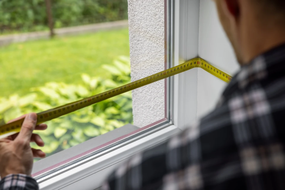 Homme en tenue de travail installant une baie vitrée coulissante à cadre anthracite dans maison en construction